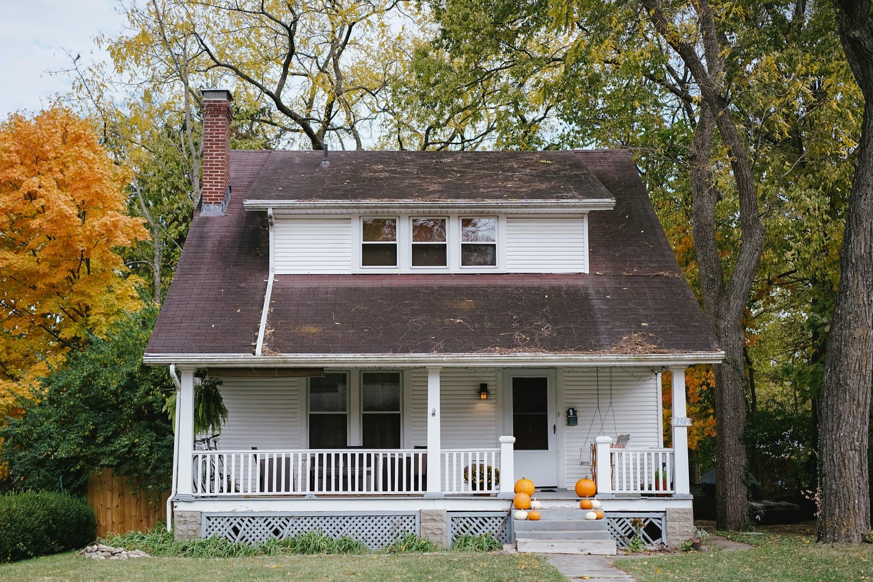 A white Craftsman-style bungalow with a covered porch, framed by autumn trees